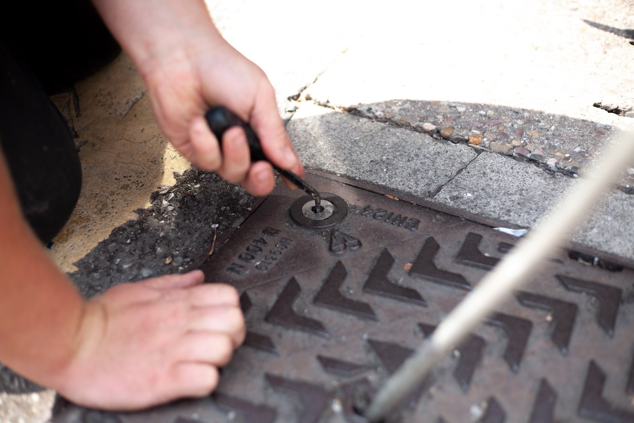 Opening manhole cover with tool. Simpsons Drainage, Drain clearance, drain unblocking, septic tank services, septic tank emptying, drain camera surveys, drain repairs, drain lining, new drains in Warminster, Frome, Trowbridge.